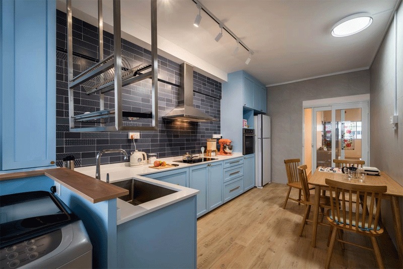 Tủ bếp gỗ công nghiệp chữ L màu xanh biển pastel vô cùng nổi bật trên nền tường bếp ốp gạch xanh đen và mặt sàn nâu gỗ